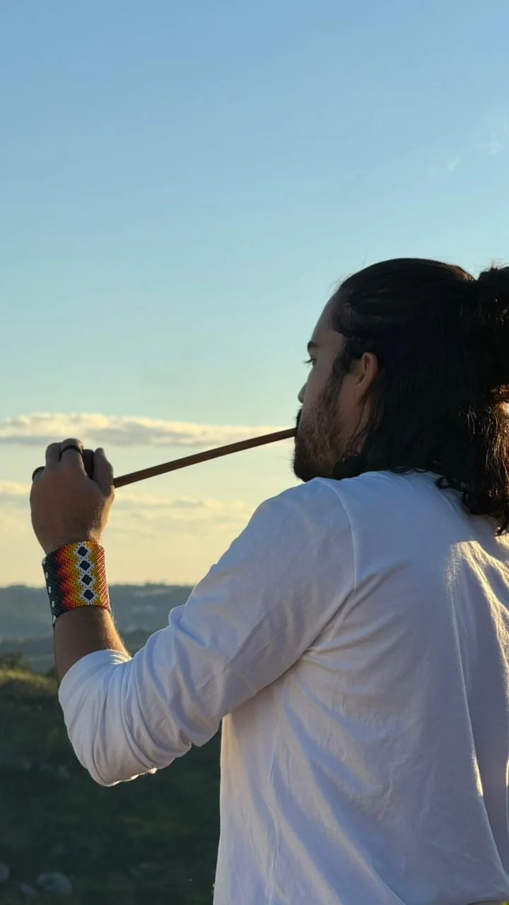 Praticante soprando a fumaça do cachimbo sagrado diante do horizonte ao entardecer